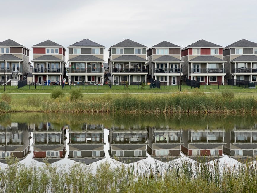 A row of modern houses reflected in a calm pond, showcasing serene suburban architecture.