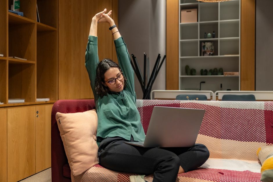 A woman relaxes while working from home on a sofa, showcasing a flexible work environment.