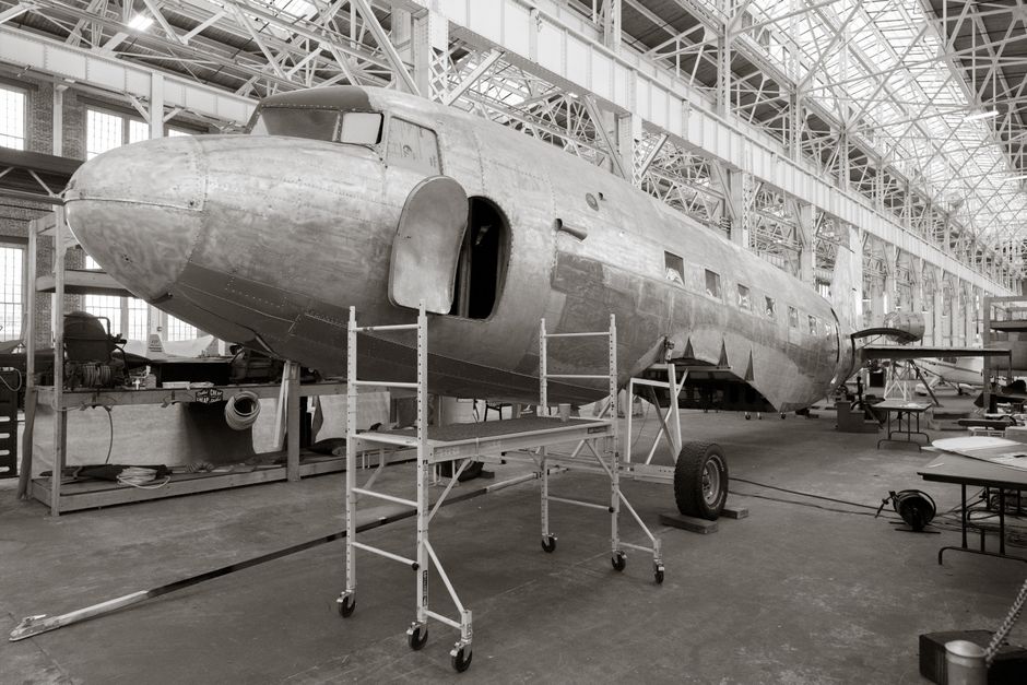 A classic aircraft undergoes restoration inside a spacious hangar, showcasing industrial architecture.