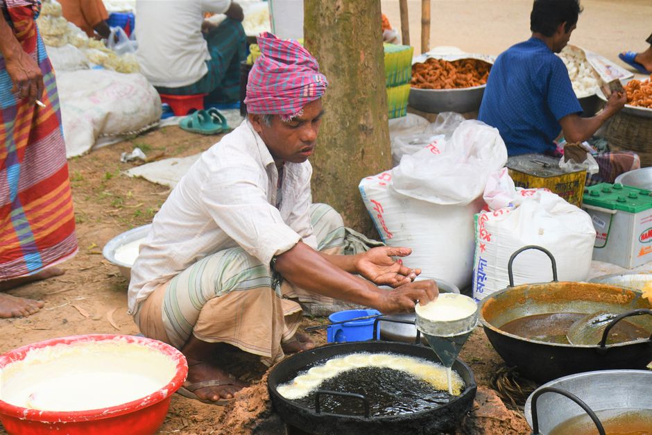 A street vendor in Rangpur, Bangladesh, frying traditional snacks at a market stall.